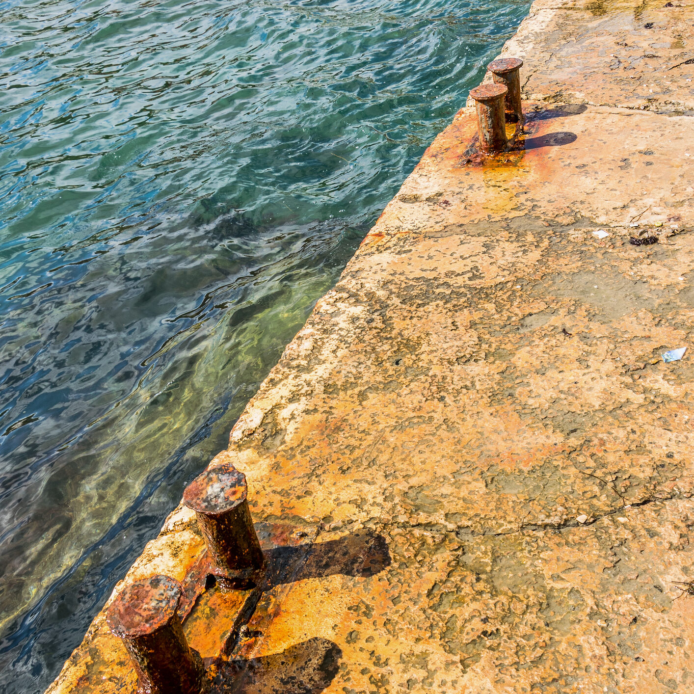 Old rusty bollards on a concrete pier. Azure sea
